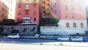 A multi-story building with balconies, a stone wall, and parked cars along the street. - Martino apartment (Genova)