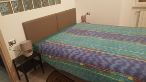 A bedroom with a bed, a nightstand, a lamp, and a radiator. - Martino apartment (Genova)
