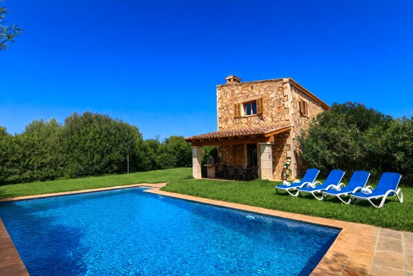 Ein Steinhaus mit Pool und blauen Liegestühlen.