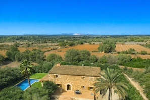 Una casa de piedra con piscina, rodeada de vegetación y campos.