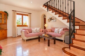 Un salón con un sofá, una mesa de centro con un tablero de ajedrez, una escalera y una ventana con cortinas.