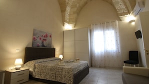 Ein Schlafzimmer mit Bett, Nachttischen, einem Gemälde, einem Sessel und einem Fenster mit Vorhängen.