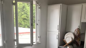 Eine kleine Küche mit weißen Schränken, einem Glastisch und einem Fenster mit geöffneten Fensterläden.