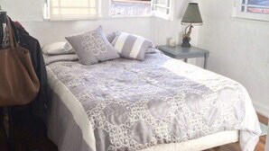 Ein Schlafzimmer mit Bett, Nachttisch, Lampe, Fenster und Blick auf Grünfläche.