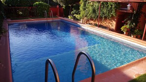 A rectangular swimming pool with clear blue water, surrounded by a red fence and potted plants.