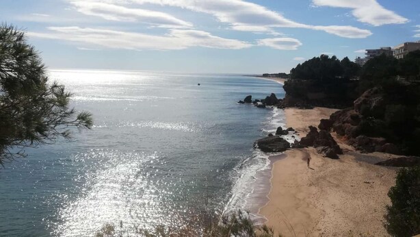 A beach with clear skies, a sandy shore, and rocky outcrops.