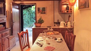 A dining area with a table set for four, a kitchen with a kettle and cups, and a door leading to a garden.