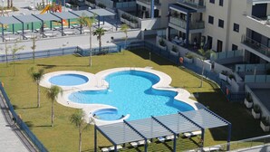 Une piscine sur le toit, divisée en plusieurs zones, entourée d’une clôture bleue et de palmiers.