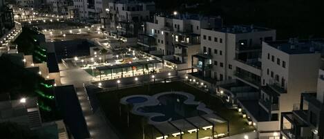 An aerial view of a residential area with modern buildings, a well-lit central square, and a sports field.