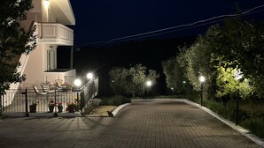 A nighttime view of a residential building with a balcony, outdoor seating, and a paved driveway.