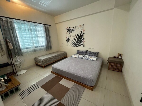 A bedroom with a bed, a bench, a fan, and a wall decoration. - Come Home Travel (Tainan)