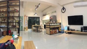 A modern living room with a sofa, a wooden coffee table, and a bookshelf. There is a TV mounted on the wall and a small table with a lamp. - Come Home Travel (Tainan)