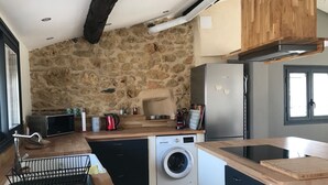 A compact kitchen with a stone wall, a washing machine, a microwave, and a refrigerator.