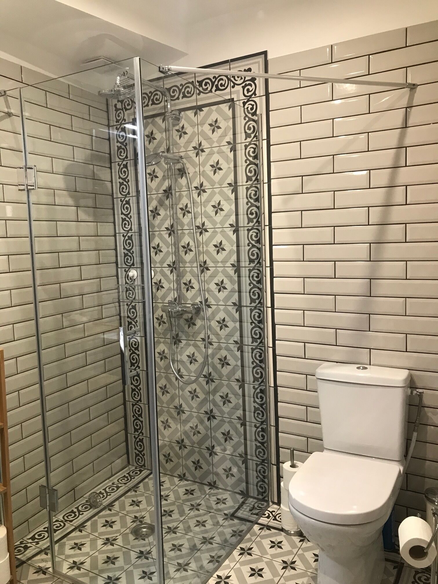 A bathroom with a glass-enclosed shower, patterned tiles, and a toilet.