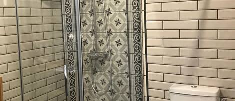 A bathroom with a glass-enclosed shower, patterned tiles, and a toilet.
