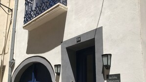 A building with two blue doors, a balcony with wrought iron railings, and a sign reading "La Jolie Vigneronne".