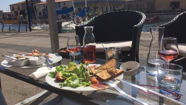 A table set with a meal, including toast, salad, and a drink, with a view of buildings and a bench in the background.