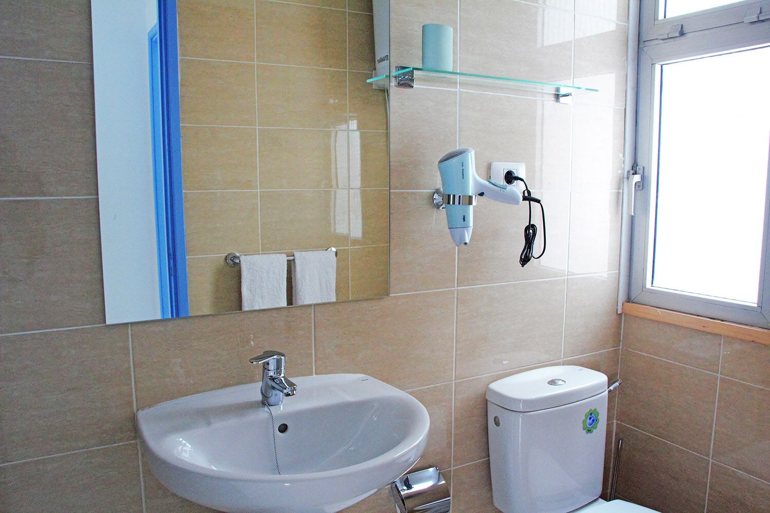 Une salle de bain équipée d’un lavabo, de toilettes et d’un sèche-cheveux fixé au mur.