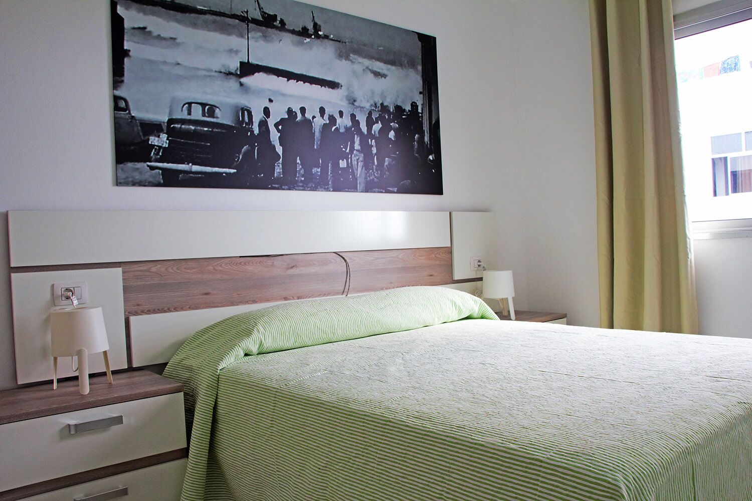 Un dormitorio con cama, mesitas de noche, lámpara de pared y un cuadro grande enmarcado sobre la cama.