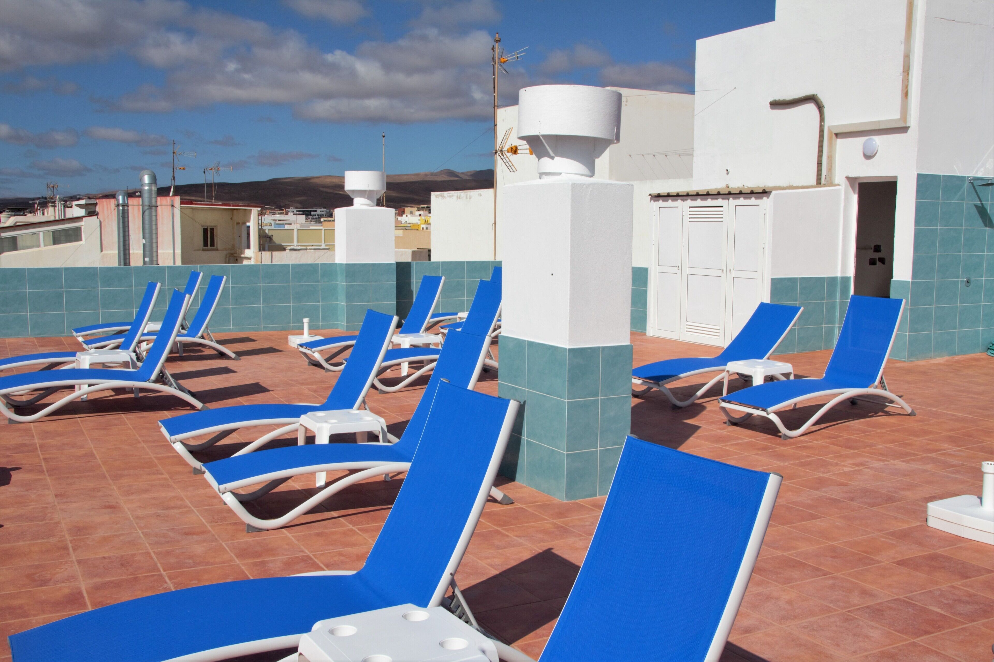 A rooftop pool area with blue lounge chairs and a white water tank.