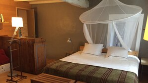 Une chambre à coucher avec un lit sous un dais, un bureau avec une lampe et un banc.