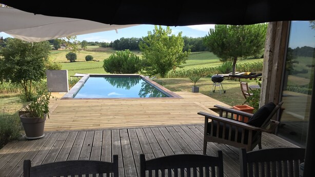 Une terrasse en bois avec une piscine, du mobilier d’extérieur et une vue sur la campagne.