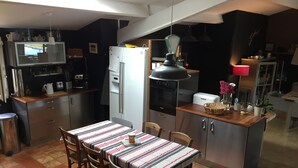 Une cuisine compacte avec un coin repas, comprenant un réfrigérateur, un four et un petit îlot central agrémenté d’une lampe.