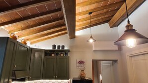 Una cocina con vigas de madera, armarios verdes, encimera blanca, lámparas colgantes y un equipo de aire acondicionado.