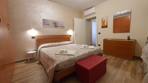 Un dormitorio con una cama, un aparador de madera, una mesita redonda y un banco rojo.