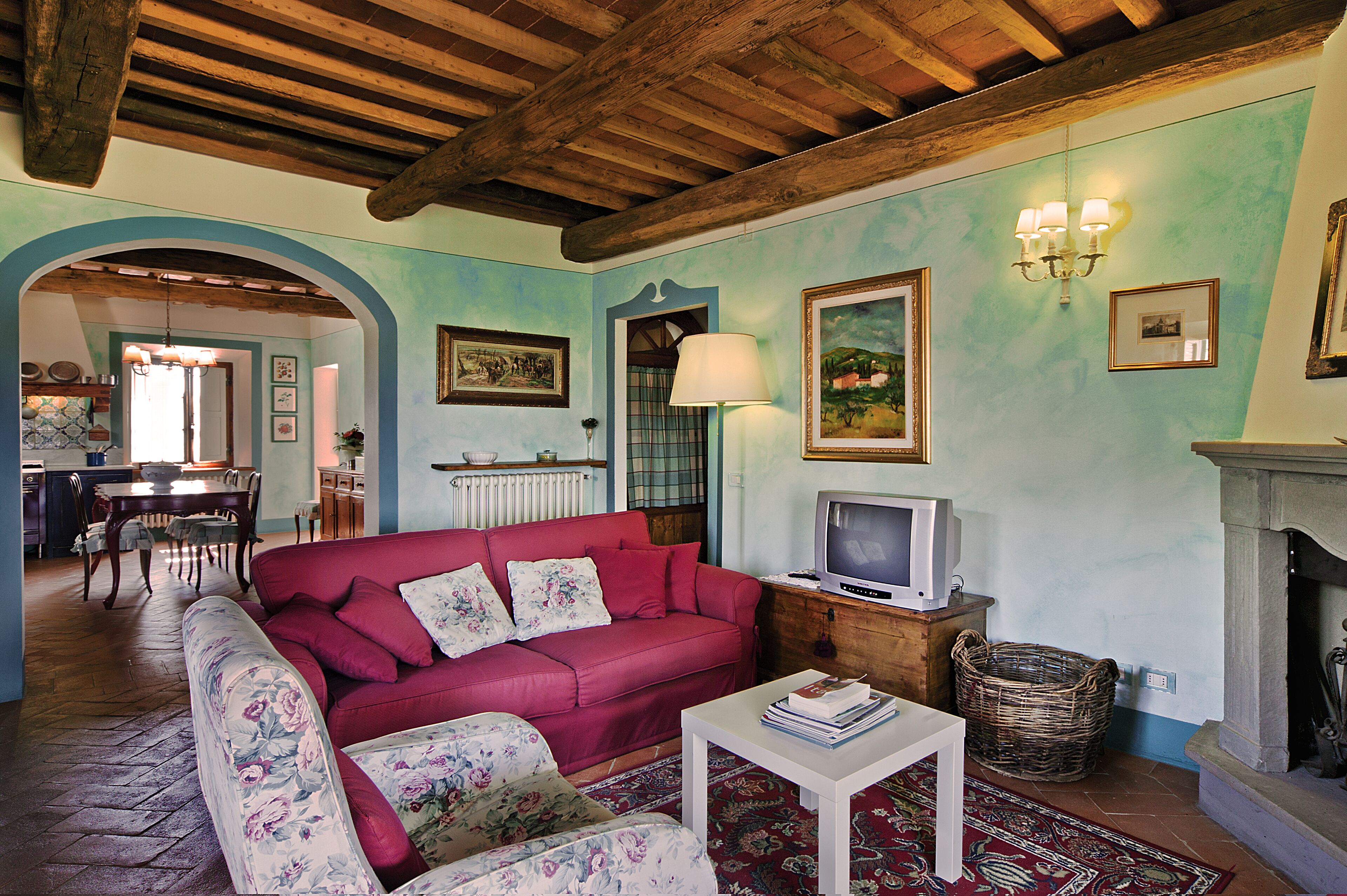 A cozy living room with a red sofa, floral armchairs, a television, and a fireplace.