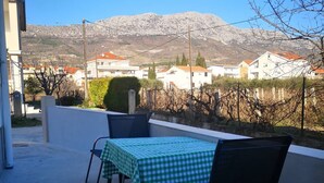 Een terras met een tafel en stoelen, met uitzicht op een woonwijk met huizen en bergen op de achtergrond.