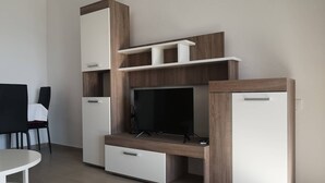 Een moderne woonkamer met een televisie, inbouwplanken en een eethoek met een tafel en stoelen.