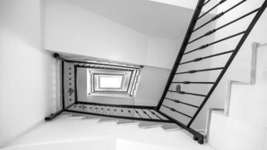 Une vue en noir et blanc d’un escalier avec une rampe métallique et un motif géométrique sur le mur.