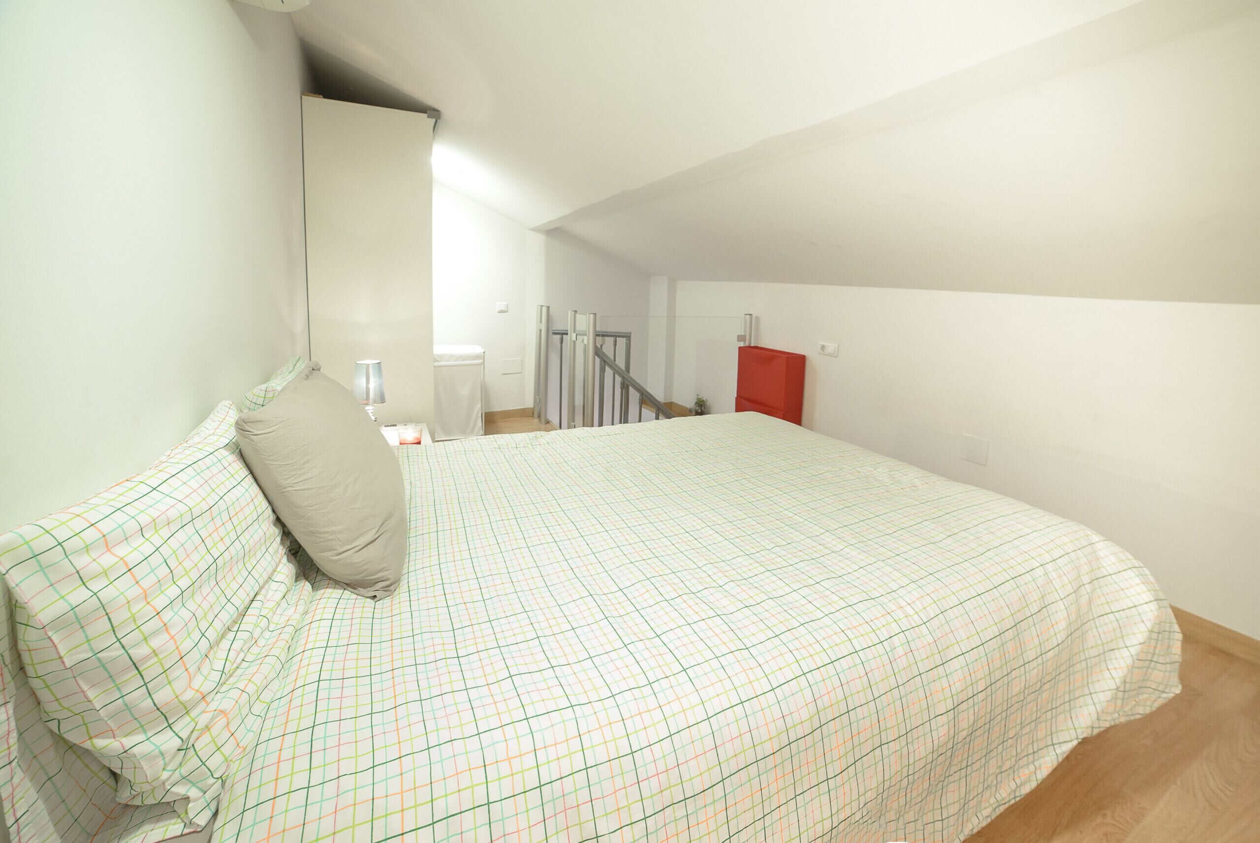 Une chambre à coucher avec un lit, une table de chevet, une armoire rouge et un escalier menant à une autre pièce.