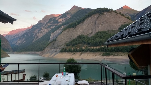 Une terrasse avec une table dressée pour le dîner, offrant une vue sur un lac et des montagnes.