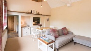 A cozy living room with a sofa, a coffee table, and a dining area with a table and chairs. - The Linhay, Kings Nympton - Quiet, very rural thatched barn near great pub. (Kings Nympton)