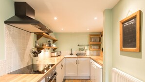 A compact kitchen with a stove, oven, and white cabinets. There is a chalkboard on the wall and a shelf with dishes. - The Linhay, Kings Nympton - Quiet, very rural thatched barn near great pub. (Kings Nympton)