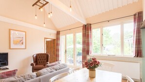 A cozy living room with a sofa, a wooden dining table, and a television. - The Linhay, Kings Nympton - Quiet, very rural thatched barn near great pub. (Kings Nympton)