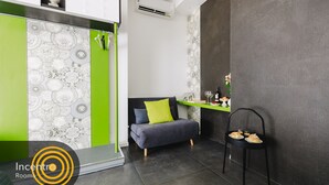 A modern room with a grey sofa, a green accent wall, a black chair, and a small table with pastries. - Incentro Rooms (Polignano a Mare)