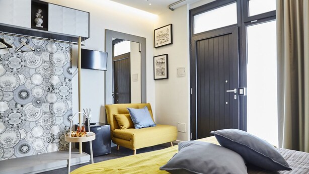 A modern hotel room with a bed, a yellow armchair, a small side table, and a patterned wallpaper. - Incentro Rooms (Polignano a Mare)
