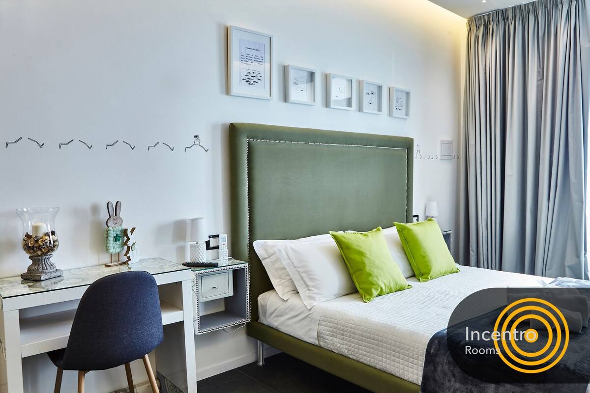 Habitación de hotel con cama, escritorio y silla. Hay cuadros en la pared y una cortina en la ventana.