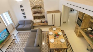 Un salon moderne comprenant un canapé, une table à manger pour quatre personnes et un coin cuisine doté d’un plan de travail et de placards en bois.