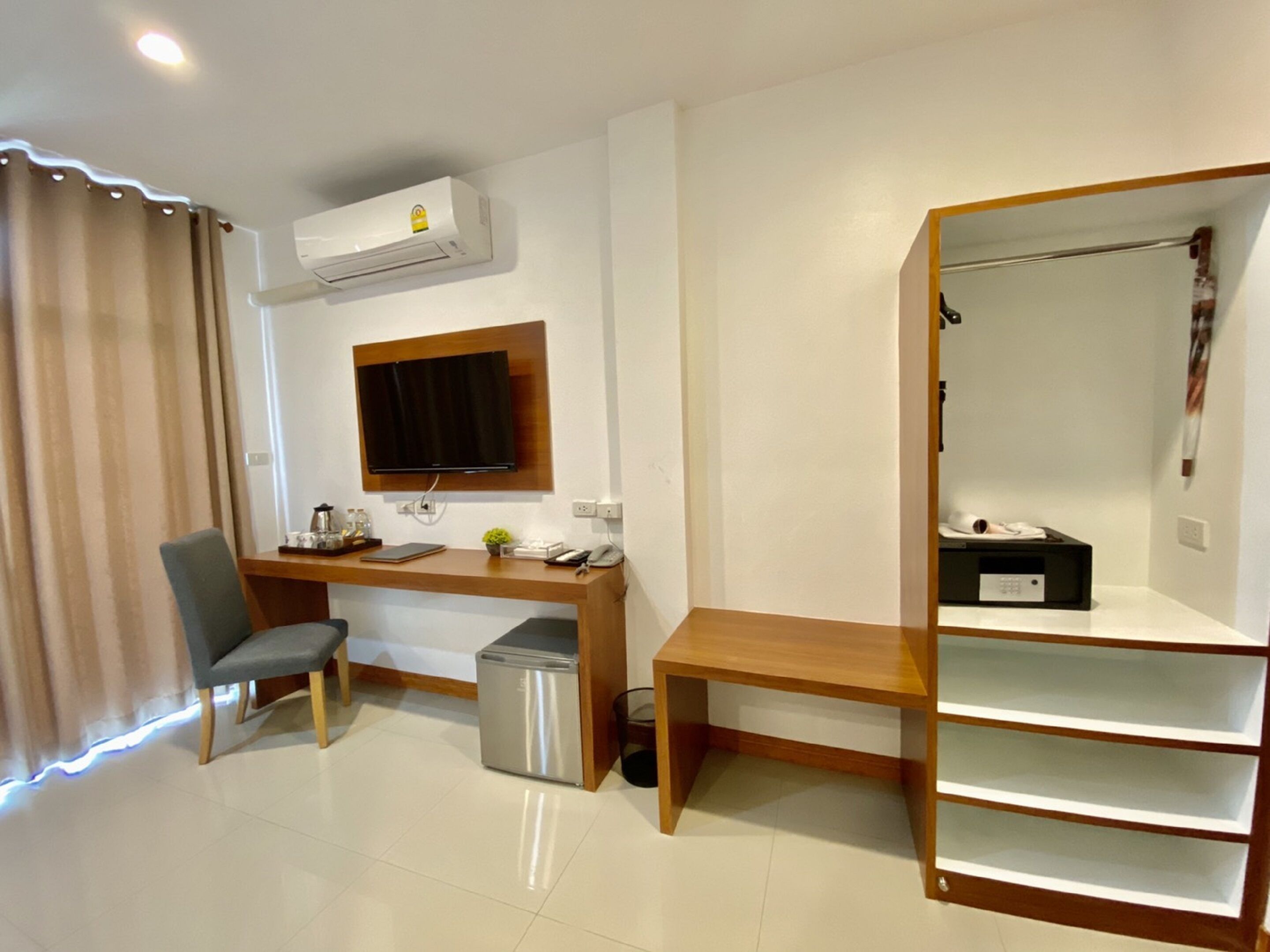A hotel room with a desk, chair, TV, air conditioning unit, and a wardrobe with shelves.