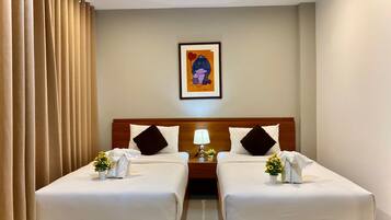 A hotel room with two beds, a wooden headboard, a framed picture on the wall, and a bedside table with a lamp and flowers.