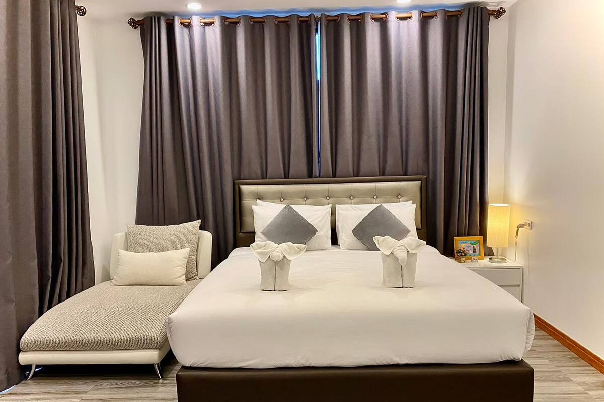 Un dormitorio ordenado con una cama grande, una mesita de noche con lámpara y un pequeño sofá.