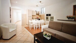 A modern living room with a sofa, a coffee table with flowers, a dining area with a white table and chairs, and a kitchen in the background. - CASA MINERVA: The Best apartment near Coloseum 5☆ (Roma)