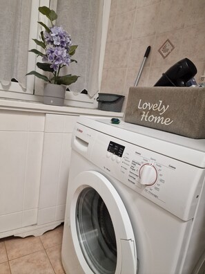 A front-loading washing machine with a control panel, a potted plant, and a 'Lovely Home' sign on a shelf. - CASA MINERVA: The Best apartment near Coloseum 5☆ (Roma)