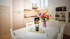A modern kitchen with white cabinets, a dining table with a wine bottle and glasses, and a vase with flowers. - CASA MINERVA: The Best apartment near Coloseum 5☆ (Roma)