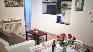 A living room with a sofa, a dining table with a vase of flowers, a small table with a decorative item, a radiator, and a door leading to another room. - CASA MINERVA: The Best apartment near Coloseum 5☆ (Roma)