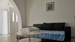 Ett modernt vardagsrum med ett runt, vitt bord, en svart soffa med en blå- och vitrutig pläd och en inramad tavla på väggen.